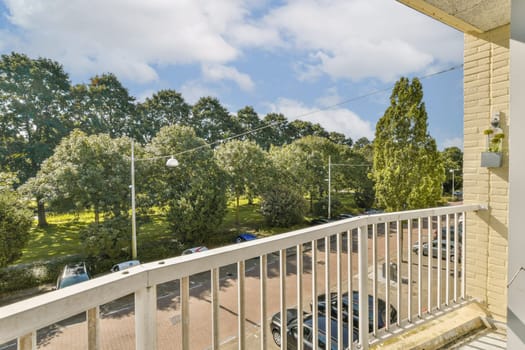 A picturesque view from a balcony, showcasing lush green trees and a well-kept park with a clear blue sky, inviting tranquility and relaxation.