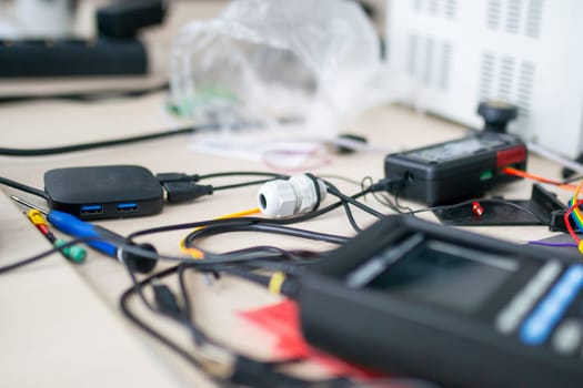 A tangled bunch of wires is currently laying messily on a table, possibly related to electronic devices or gadgets nearby