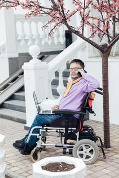 Man in a wheelchair working with a laptop online negotiating on the phone