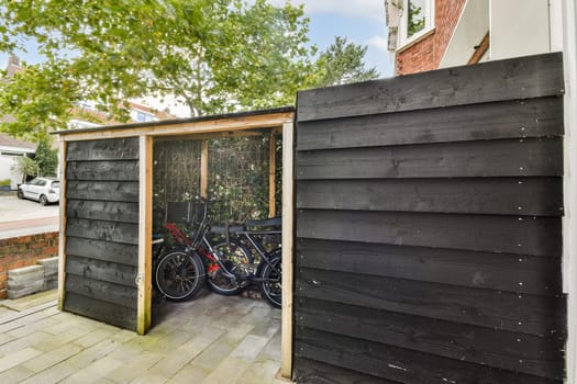 A sleek bicycle storage shed made from dark wooden planks, set in a suburban neighborhood with greenery in the background.