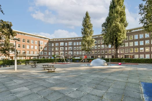 A vibrant playground surrounded by residential buildings featuring play equipment and green spaces for children and families. A sunny day enhances the lively atmosphere.