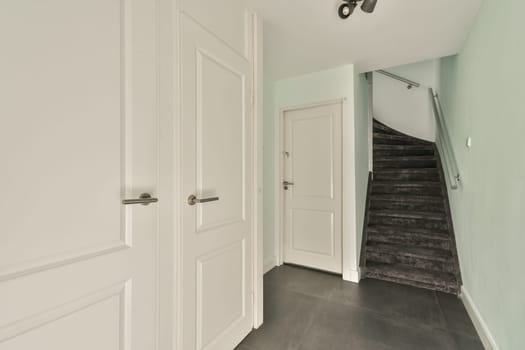 A sleek entrance featuring white doors and a modern staircase, complemented by soft green walls and dark flooring that enhances the overall ambiance.