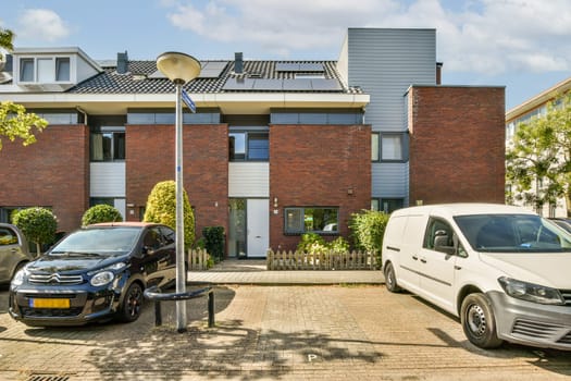 A contemporary residential building featuring a brick facade and several parked cars in an urban setting, highlighted by clear blue skies.