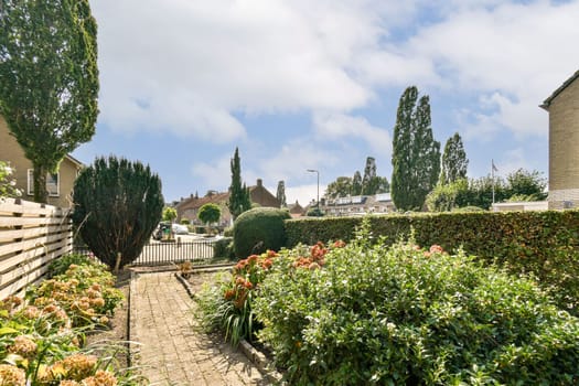 A serene garden pathway is framed by lush greenery and vibrant flowers, leading through a peaceful residential area under a clear blue sky.