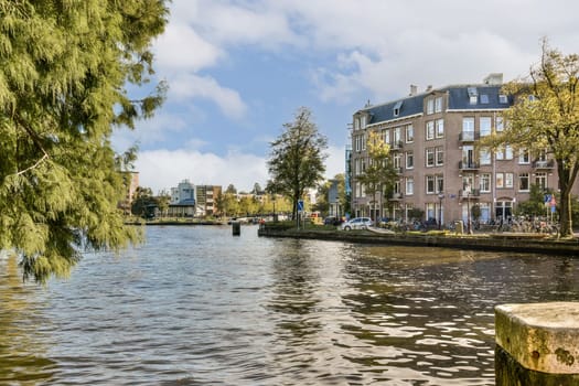 A peaceful canal scene surrounded by trees, showcasing historic buildings on one side and vibrant autumn colors reflecting in the water. Ideal for nature enthusiasts.