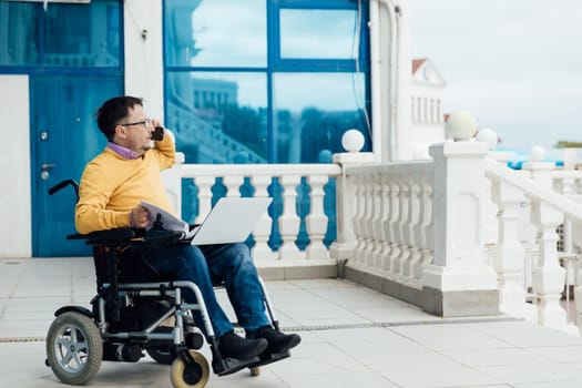 Man in a wheelchair working with a laptop online negotiating on the phone