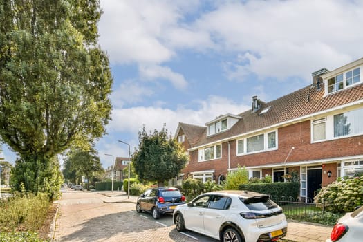 Tree-lined street showcasing contemporary houses and parked cars, filled with greenery and warm sunlight creating a welcoming atmosphere.