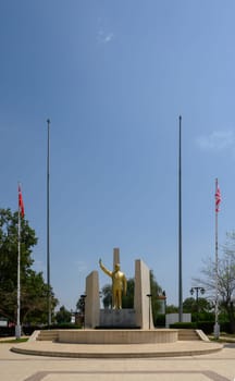 Golden statue of Mustafa Kemal Ataturk, the founder of modern Turkey, located in a public square in Northern Cyprus. The statue is flanked by flagpoles with Turkish and Turkish Republic of Northern Cyprus (TRNC) flags. Clear blue sky and surrounding park area complete the scene