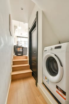A stylish laundry area featuring a washing machine near wooden stairs, blending functionality with contemporary design.