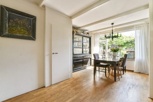 A stylish dining room featuring a wooden floor, elegant chandelier, and a blend of modern and classic furniture, creating a warm atmosphere.