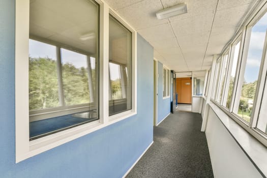 A spacious corridor featuring large windows that allow natural light to flood in, complemented by blue walls and modern architecture. Ideal for showcasing contemporary design.
