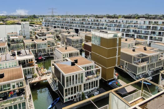 Aerial view of a contemporary housing development by the water showcasing stylish architecture surrounded by serene nature and vibrant community life.