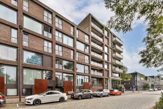 The image showcases a contemporary apartment building with large windows and greenery nearby, set against a cloudy sky. A stylish urban environment is depicted.