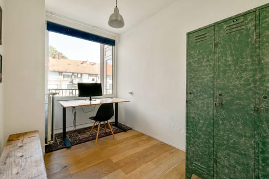 A stylish modern workspace featuring a simple desk setup, green lockers, and a view of neighboring buildings. The decor promotes productivity and comfort.