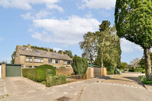 A beautiful residential house nestled among green trees with a well-kept garden and driveway under a bright blue sky.