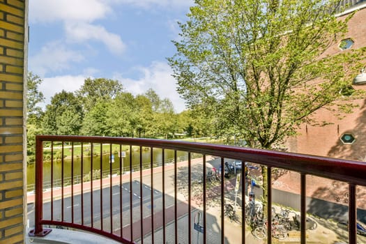 A serene scene captured from a balcony, showcasing lush trees, a pathway, and a tranquil body of water under a clear blue sky. Ideal for nature lovers and urban tranquility.