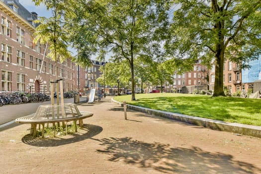 A vibrant urban park in Amsterdam features modern wooden benches surrounded by greenery and brick buildings, showcasing a blend of nature and architecture.