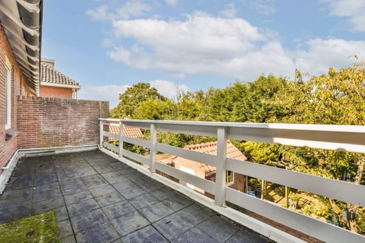 A spacious modern balcony offers an expansive view of lush greenery and a bright blue sky, creating a serene outdoor retreat for relaxation and enjoyment.
