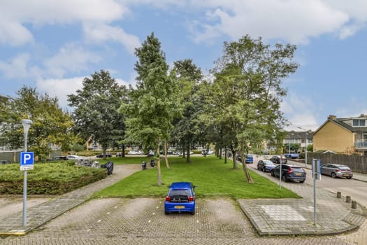 A serene urban park scene featuring green trees, parked cars, and people walking, creating a tranquil atmosphere in the city.