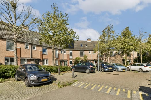 A view of a residential parking area featuring multiple parked cars surrounded by grassy patches and trees under a clear blue sky.