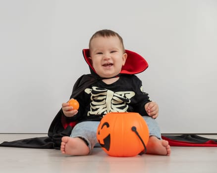 Cute caucasian boy in dracula halloween costume holding candy basket on white background