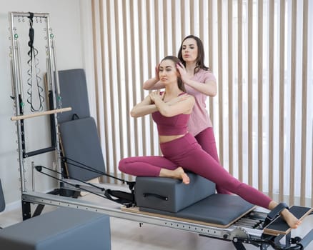 Personal Pilates training. Instructor adjusts woman on reformer
