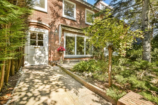 A picturesque outdoor scene featuring a brick house surrounded by lush greenery, flowers, and a charming pathway leading to the entrance.