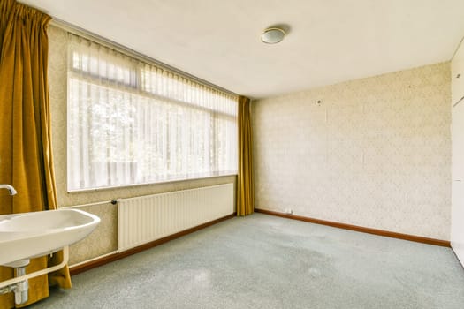 A spacious room featuring large windows with soft curtains, a wall-mounted radiator, and simple design elements creating a bright atmosphere.