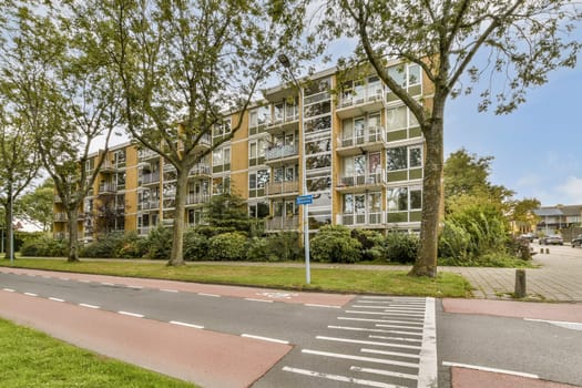 A modern apartment building featuring multiple balconies, framed by lush trees and a well-maintained road, showcasing a blend of nature and urban living.