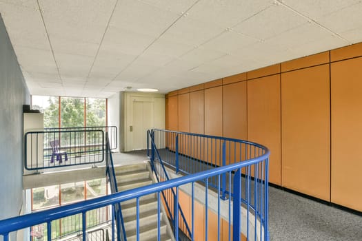 A modern indoor staircase featuring a curved railing, natural light streaming through large windows, and an orange accent wall, creating a inviting atmosphere.