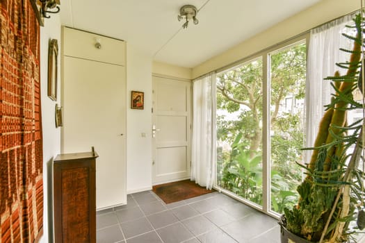 A modern entrance space featuring large windows that let in abundant natural light, a potted plant, and elegant decor, creating a welcoming atmosphere.