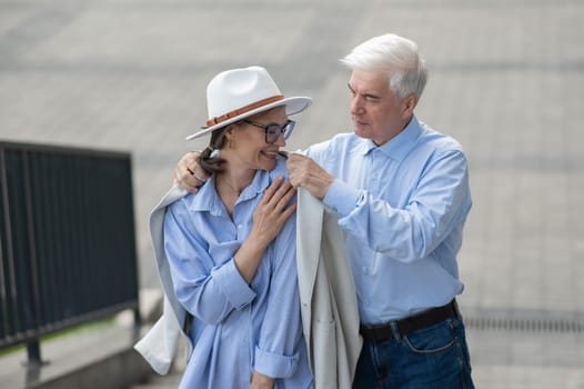 An elderly man puts his jacket on a woman. Romantic relationships of mature people