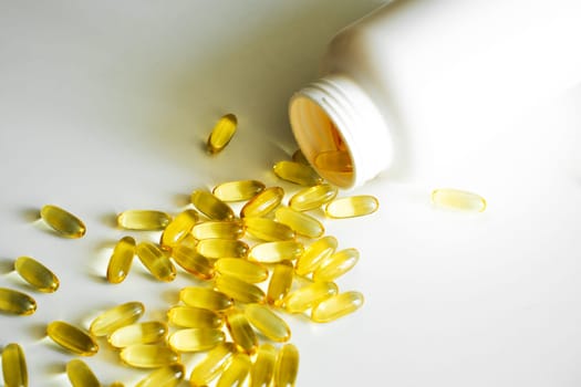 Gel capsules omega-3 laying near a white bottle on white background. Nutritional supplement