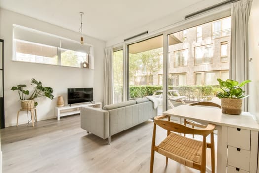 Bright and spacious living room featuring a comfortable sofa, a television, and lush greenery outside the large windows, creating a serene atmosphere.