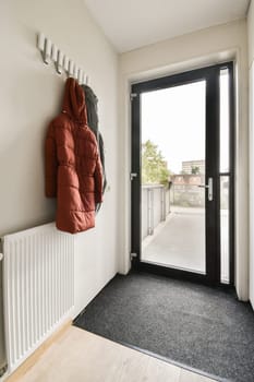A contemporary entrance hall showcasing a coat rack with a bright red jacket, a doormat, and a large door leading to an outdoor space.