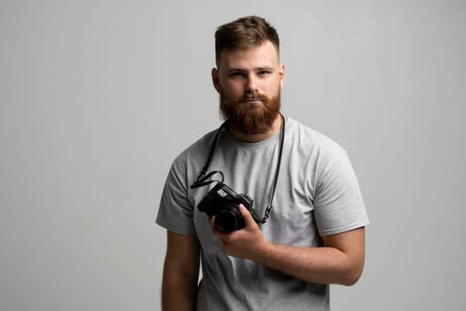 Portrait of bearded professional photographer with photo camera looks straight into the camera