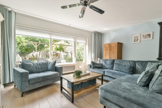 A bright and airy living room featuring soft blue furnishings, stylish decor, wooden flooring, and large windows that invite natural light.