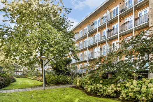 A contemporary residential building features balconies overlooking a beautifully landscaped garden with vibrant plants and trees, enhancing the serene atmosphere.