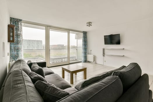 A stylish, contemporary living room featuring a cozy sofa, wooden coffee table, and large windows that offer an expansive view of the outside.