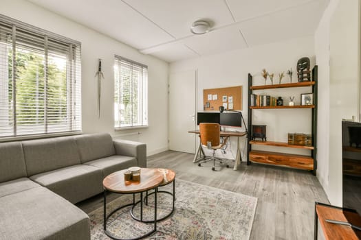 A sleek and cozy minimalist living room featuring a gray sofa, wooden desk, and decorative shelving. Natural light filters through the windows, enhancing the serene ambiance.