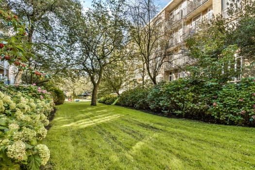 A vibrant garden featuring lush greenery and well-maintained lawns, adjacent to a charming residential building under a clear sky.