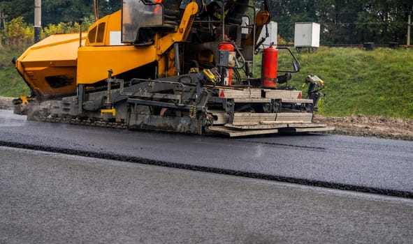 Asphalt paver machine laying fresh asphalt on road construction site