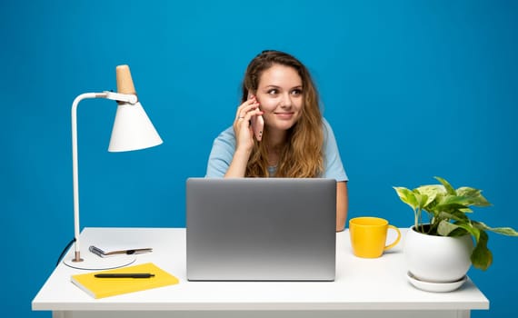Young woman speaking mobile phone and looking in laptop