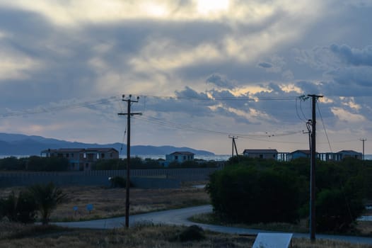 A tranquil coastal landscape unfolds during dusk, with gentle waves lapping against the shore. The sky is filled with soft clouds and a warm golden light. Distant mountains create a serene backdrop.