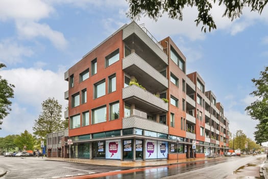 A striking modern building design featuring large windows and balconies, complemented by vibrant retail signage at the base, situated in an urban environment.