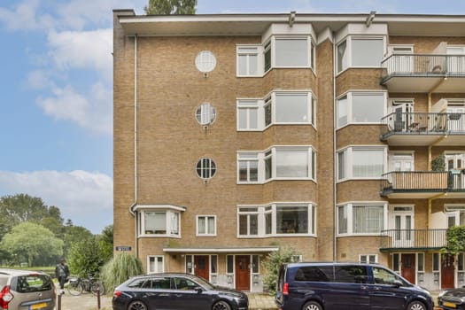 A contemporary apartment structure featuring large windows and a well-maintained exterior situated in an urban environment near greenery.
