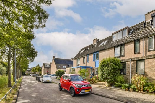 A scenic view of a residential area featuring modern buildings, parked cars, and green trees lining the street. The vibrant red car stands out against the backdrop.