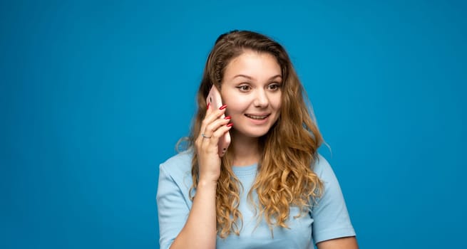 Portrait of a beautiful young woman talking on the phone on blue background