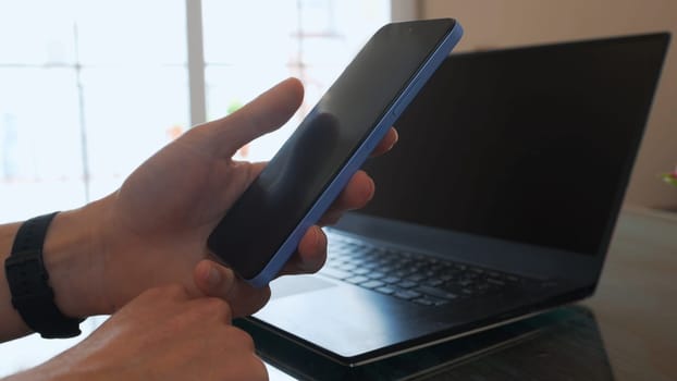 A person interacts with a smartphone while placed near a laptop, capturing modern technology usage in a personal or professional setting, emphasizing productivity and connectivity.