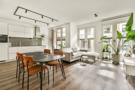 Contemporary living area featuring a sleek dining table, stylish chairs, and large windows for natural light. A green plant adds a touch of nature to the urban setting.